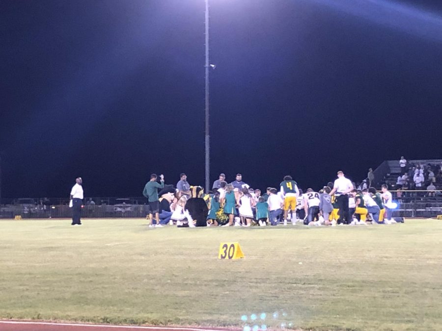 SE and Happy Cheerleaders, football players, and coaches taking a knee with each other after the game.