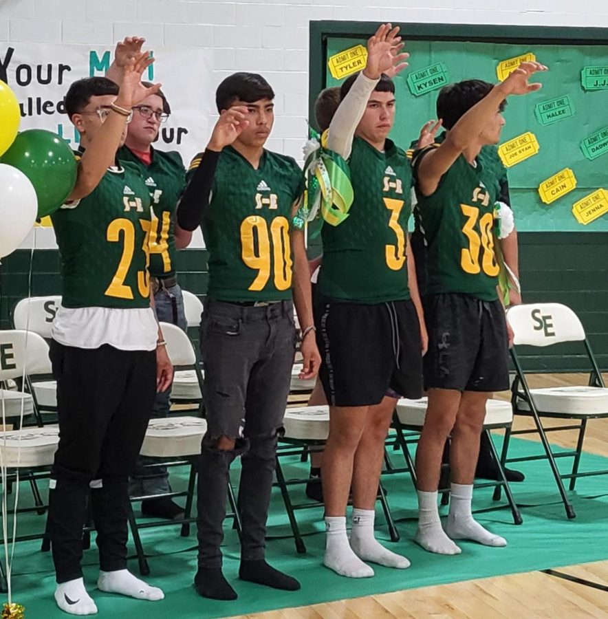 Varsity football players raising their Wolverine paws during the school song.